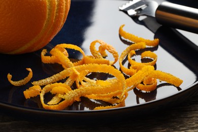 Photo of Fresh orange zest, fruit and zester on wooden table, closeup