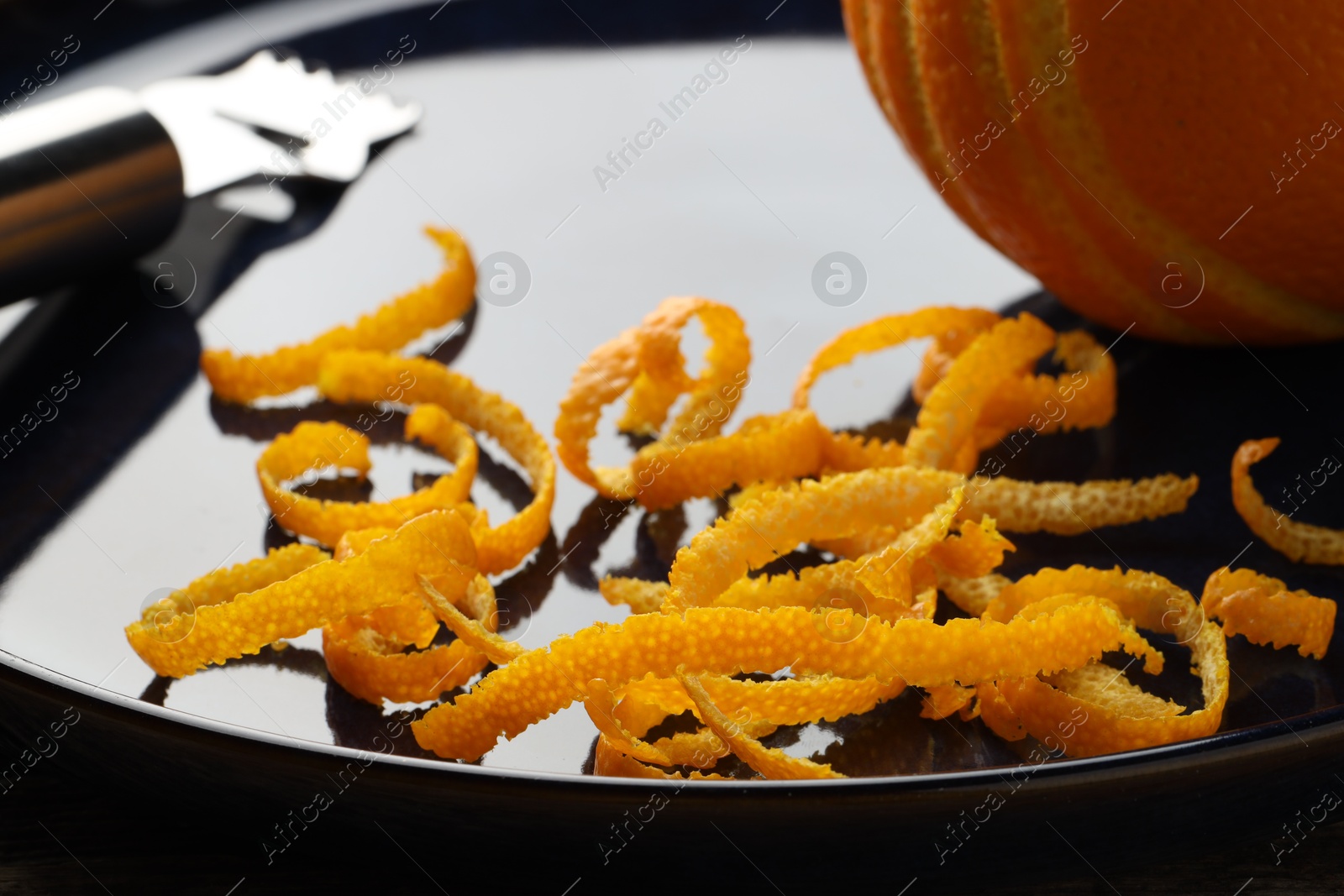 Photo of Fresh orange zest, fruit and zester on plate, closeup