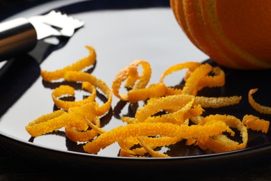 Photo of Fresh orange zest, fruit and zester on plate, closeup