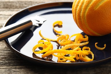 Fresh orange zest, fruit and zester on wooden table, closeup