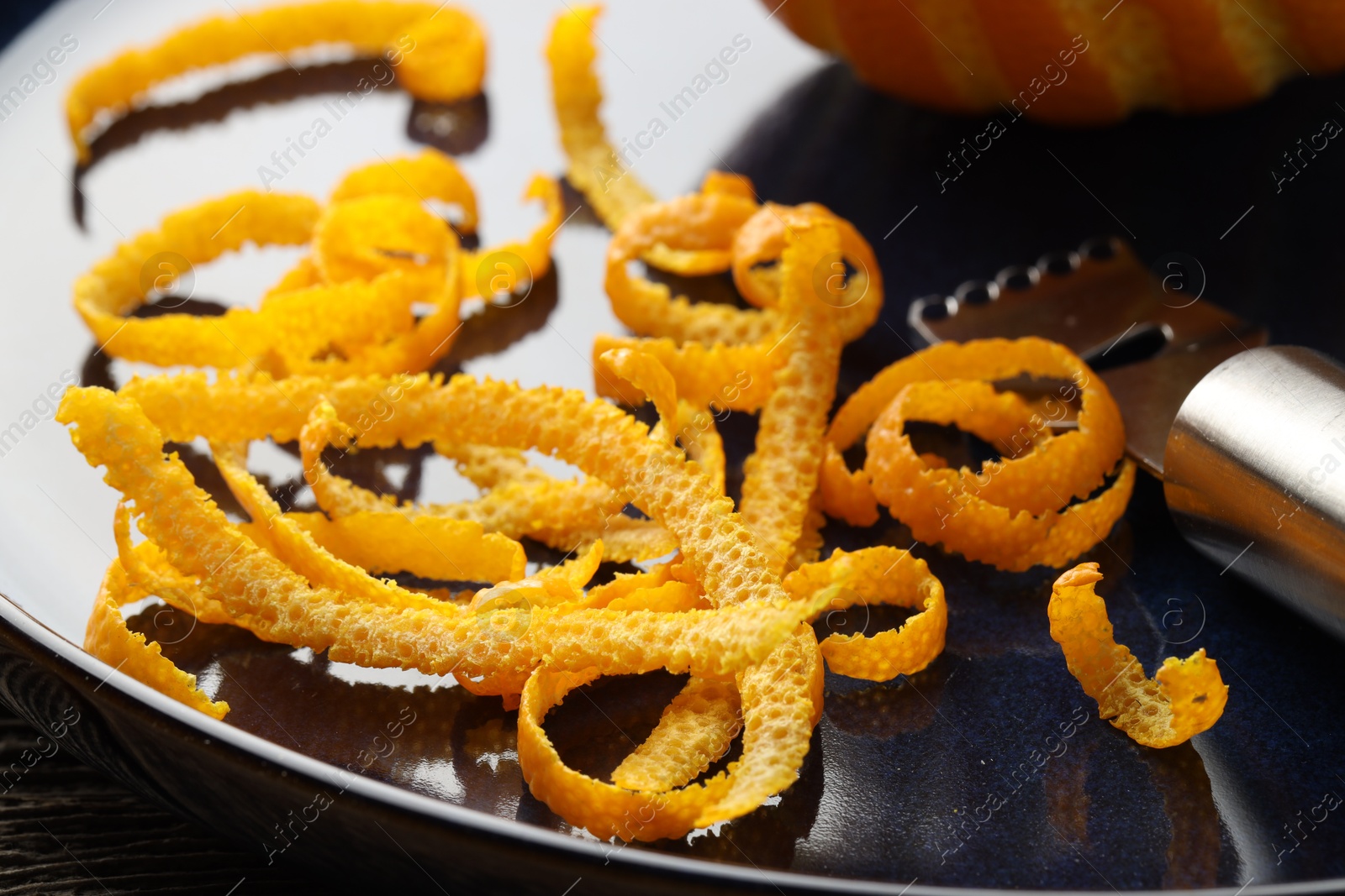 Photo of Plate with fresh orange zest and zester on table, closeup