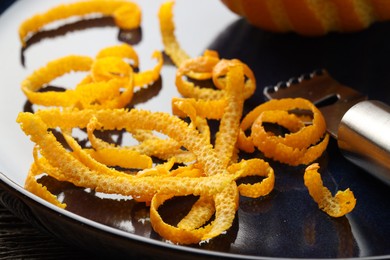 Photo of Plate with fresh orange zest and zester on table, closeup