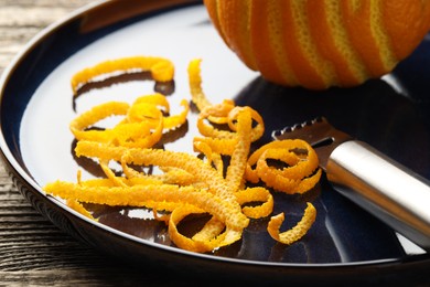 Fresh orange zest, fruit and zester on wooden table, closeup