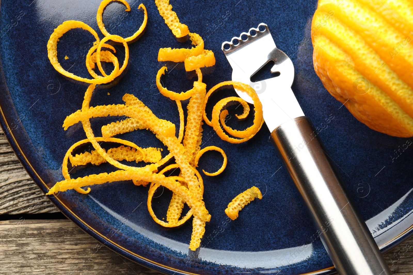 Photo of Fresh orange zest, fruit and zester on wooden table, flat lay