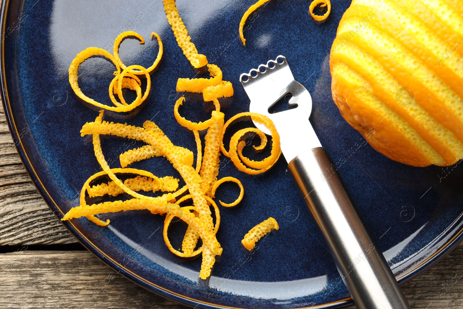 Photo of Fresh orange zest, fruit and zester on wooden table, flat lay