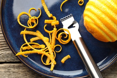 Photo of Fresh orange zest, fruit and zester on wooden table, flat lay