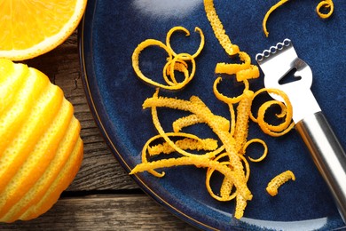 Photo of Fresh orange zest, fruits and zester on wooden table, flat lay