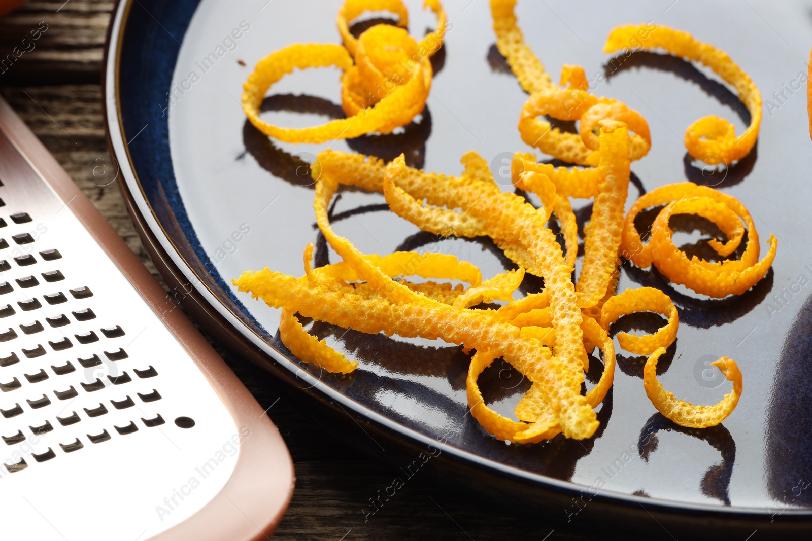 Photo of Fresh orange zest and grater on wooden table, closeup