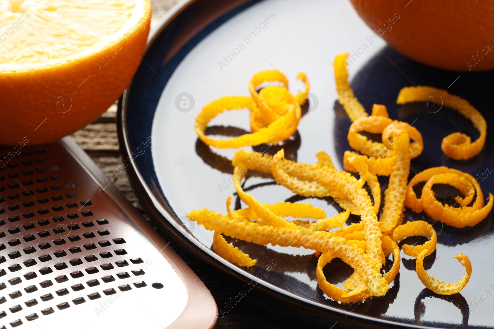 Photo of Fresh orange zest, fruits and grater on wooden table, closeup