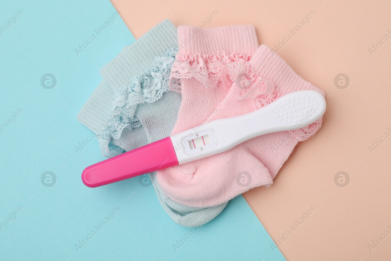 Photo of Pregnancy test and baby socks on color background, flat lay