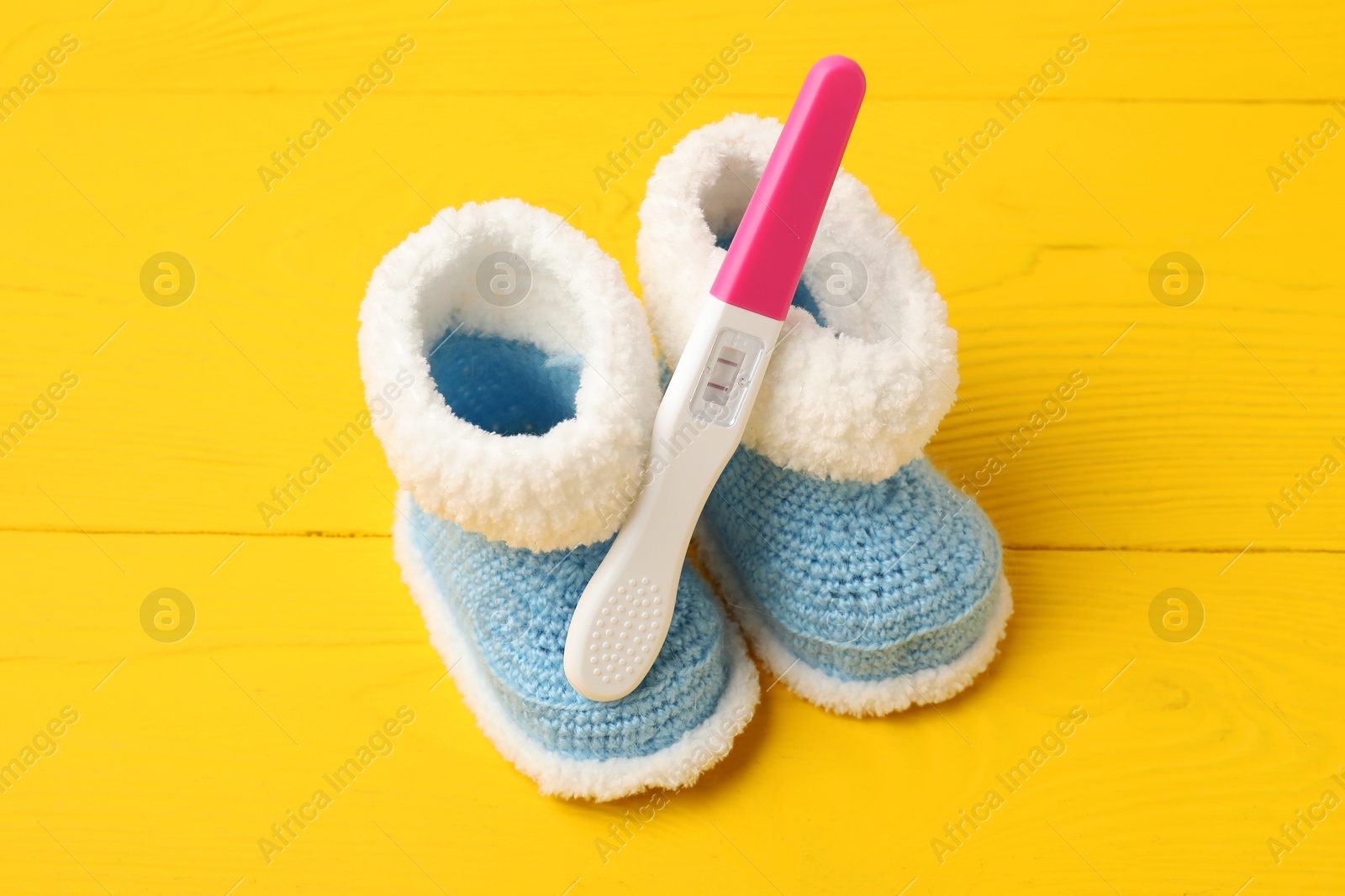 Photo of Pregnancy test and baby shoes on yellow wooden table