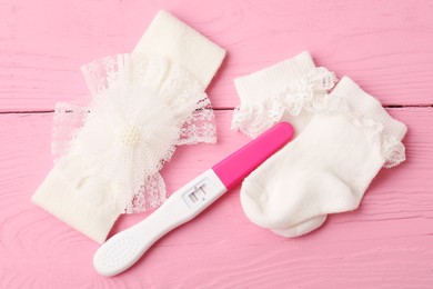 Photo of Pregnancy test and baby socks on pink wooden table, flat lay