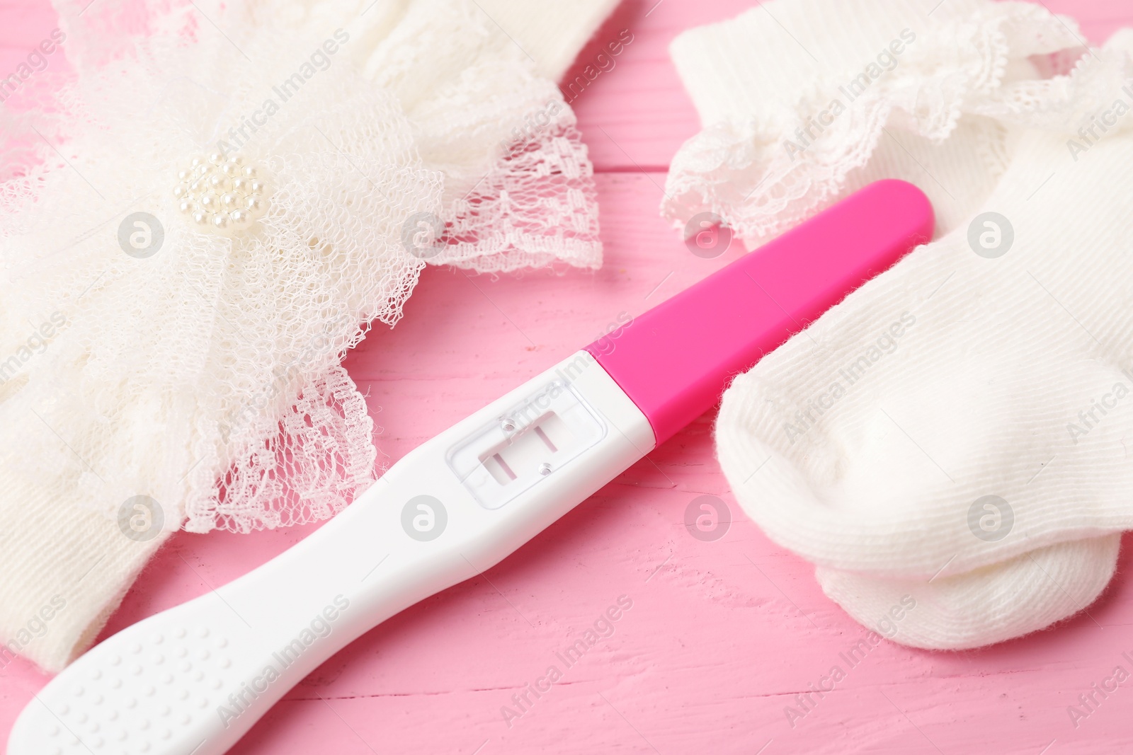 Photo of Pregnancy test and baby socks on pink wooden table, closeup