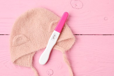 Photo of Pregnancy test and baby hat on pink wooden table, top view. Space for text