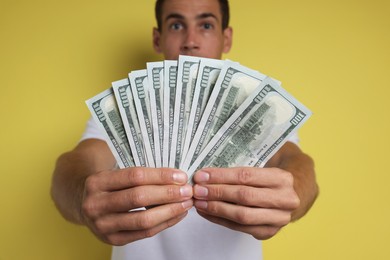 Man with dollar banknotes on yellow background, selective focus