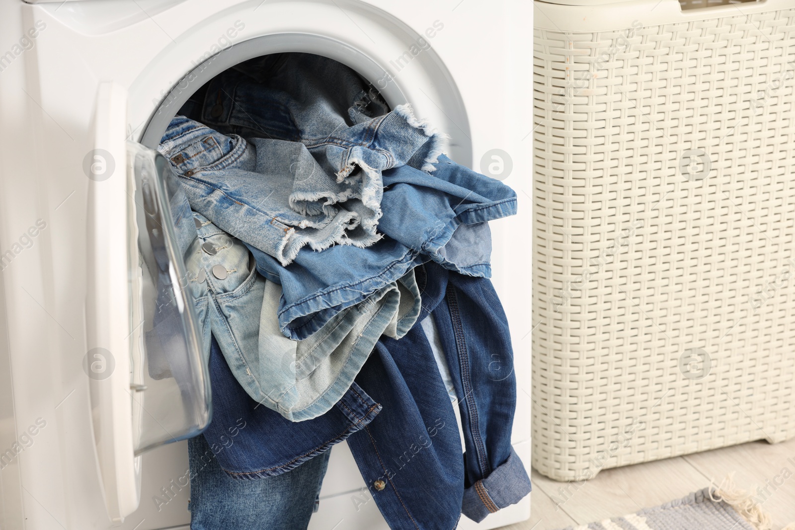 Photo of Washing machine with dirty jeans and other denim clothes indoors