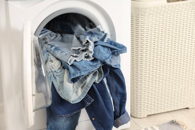 Photo of Washing machine with dirty jeans and other denim clothes indoors