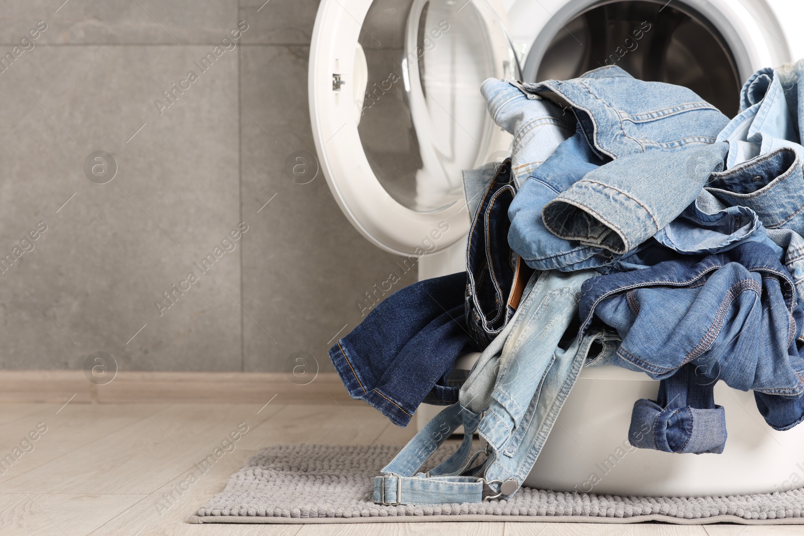 Photo of Washing machine and laundry basket with dirty denim clothes indoors, space for text