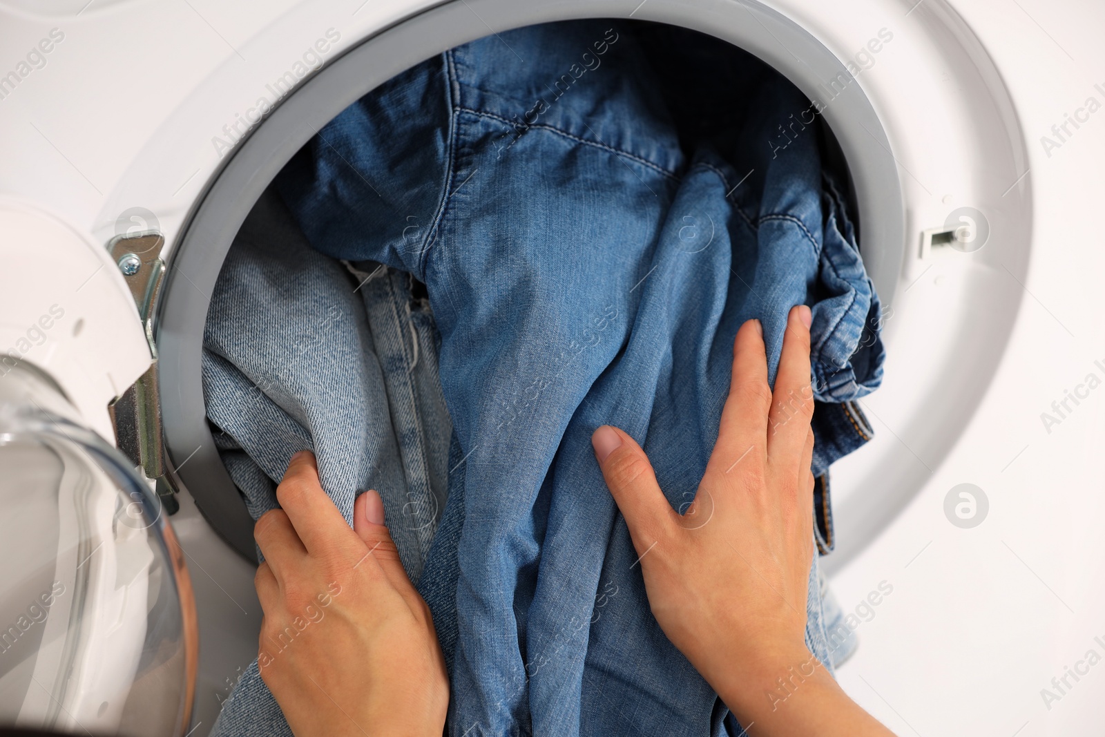 Photo of Woman putting dirty jeans and other denim clothes into washing machine, closeup