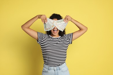 Photo of Happy woman covering eyes with dollar banknotes on yellow background