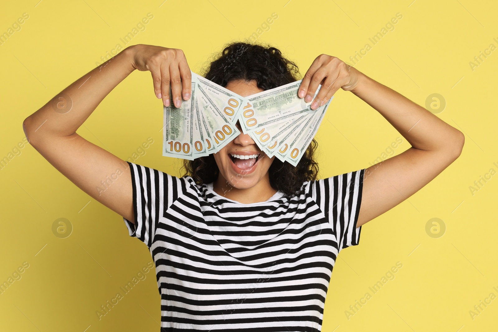 Photo of Happy woman covering eyes with dollar banknotes on yellow background