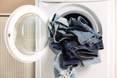 Photo of Washing machine with dirty jeans and other denim clothes indoors