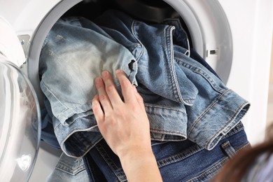 Photo of Woman putting dirty jeans and other denim clothes into washing machine, closeup