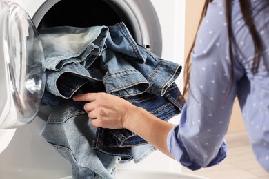 Woman putting dirty jeans and other denim clothes into washing machine, closeup