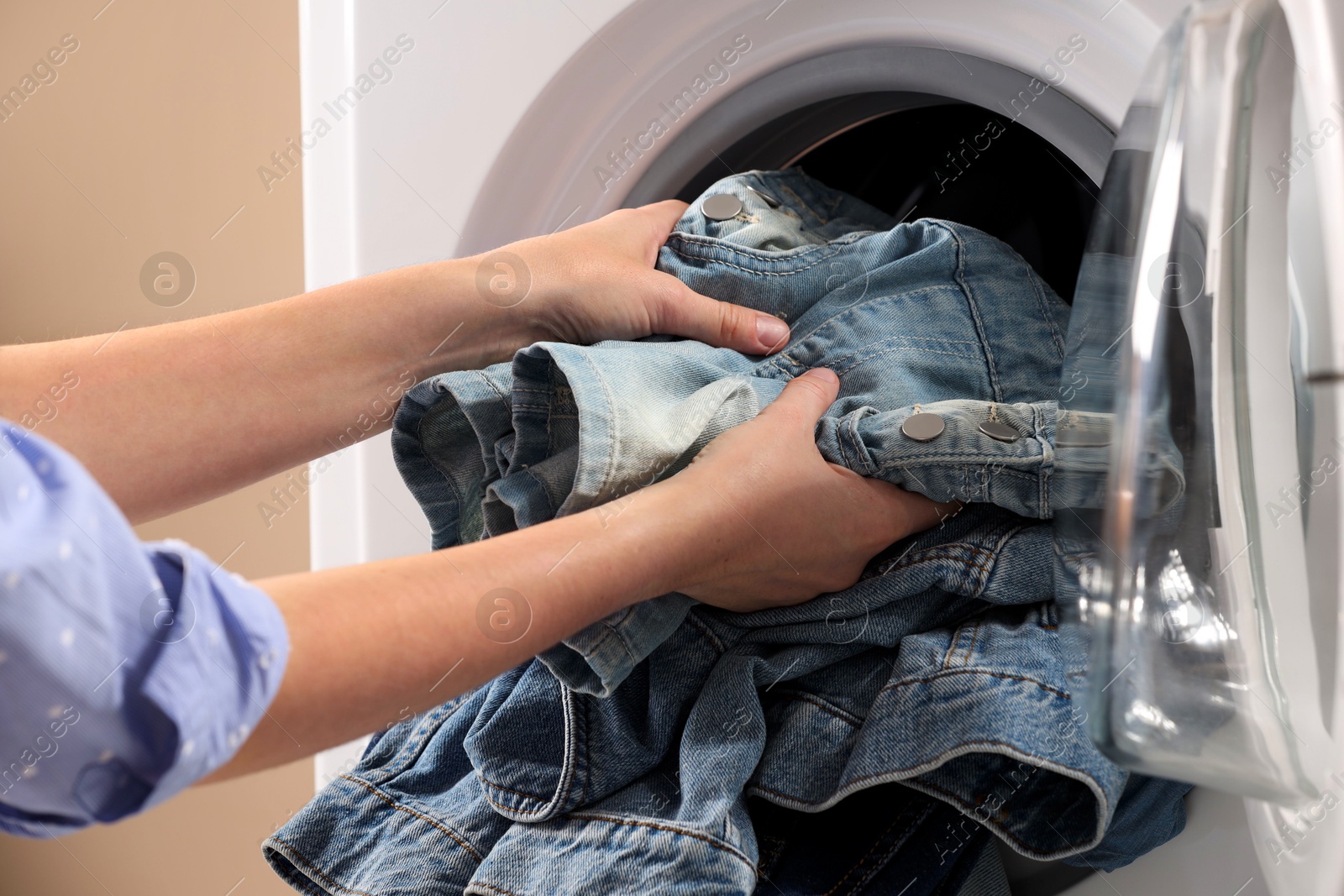 Photo of Woman putting dirty jeans and other denim clothes into washing machine, closeup