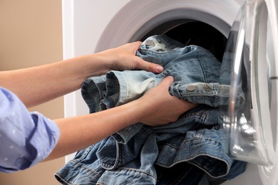 Woman putting dirty jeans and other denim clothes into washing machine, closeup