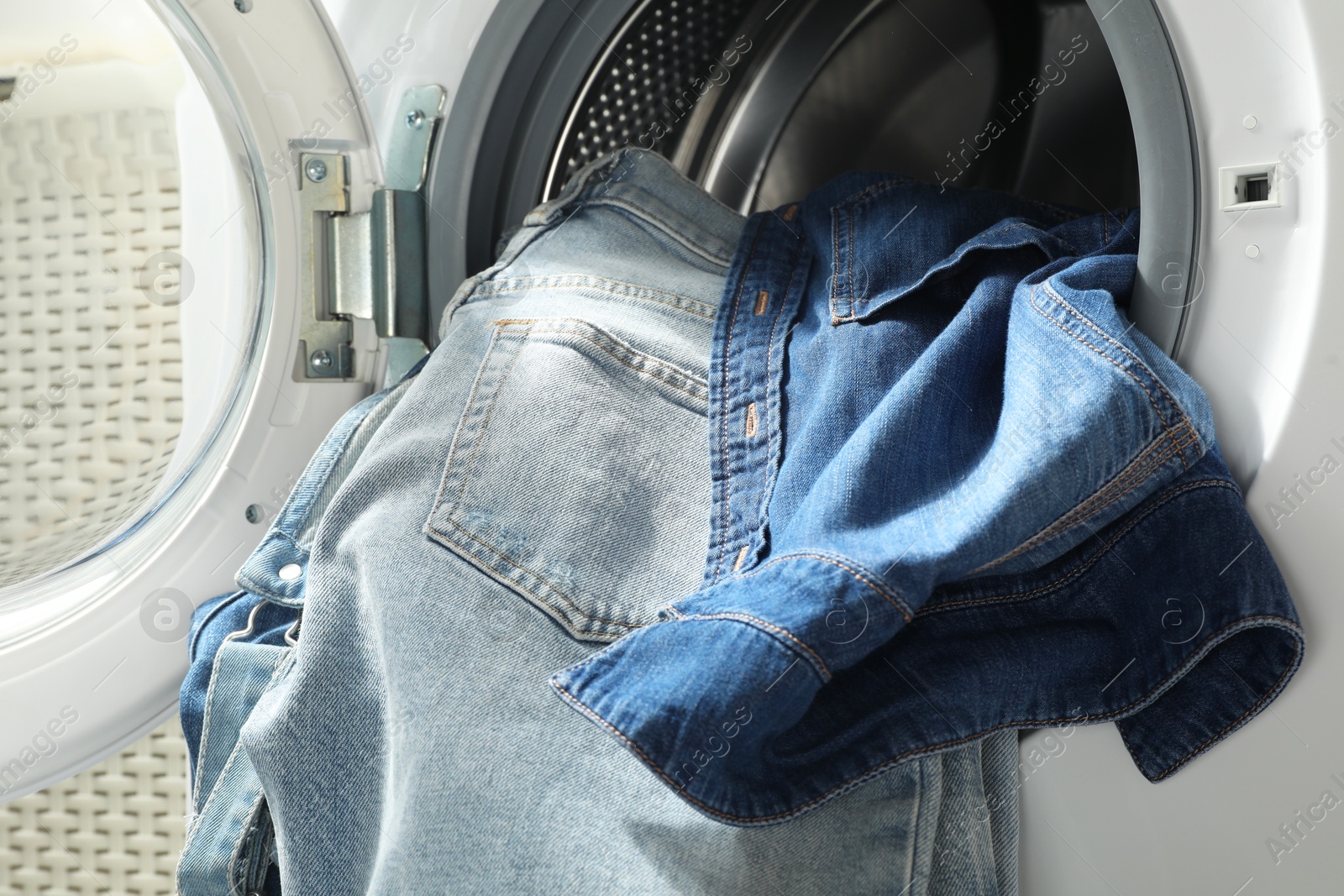 Photo of Washing machine with dirty jeans and other denim clothes indoors, closeup