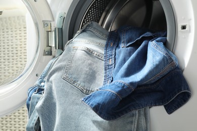 Washing machine with dirty jeans and other denim clothes indoors, closeup