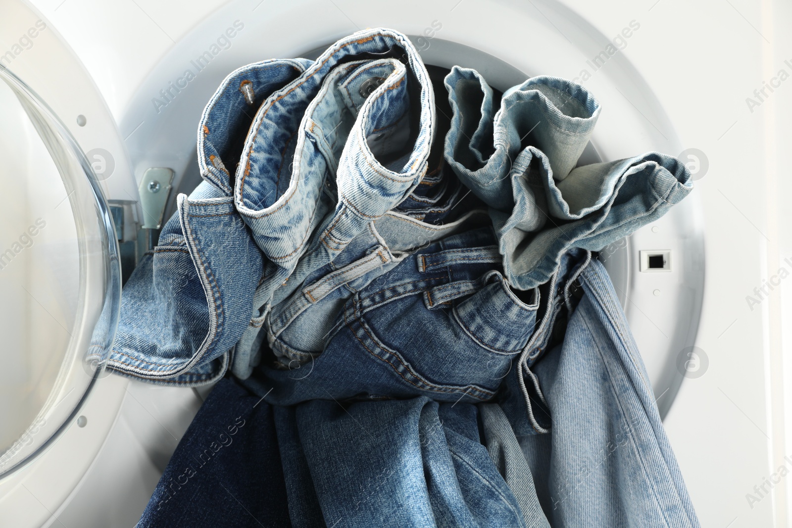 Photo of Washing machine with dirty jeans and other denim clothes indoors, closeup