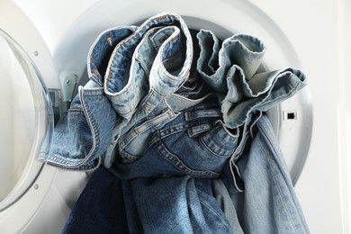 Photo of Washing machine with dirty jeans and other denim clothes indoors, closeup