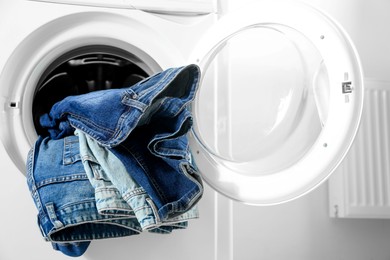 Photo of Washing machine with dirty jeans and other denim clothes indoors, closeup