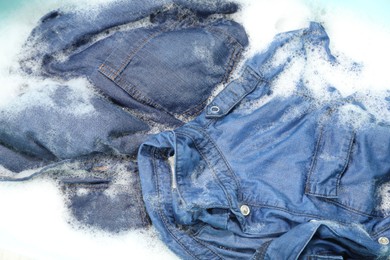 Photo of Many different denim clothes in basin with water and soap, top view