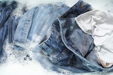 Photo of Many different denim clothes in basin with water and soap, top view