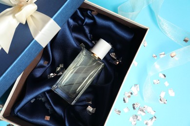 Photo of Perfume bottle in gift box and confetti on light blue background, top view