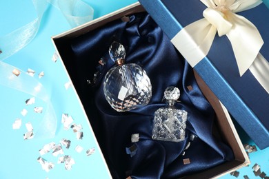 Perfume bottles in gift box and confetti on light blue background, top view