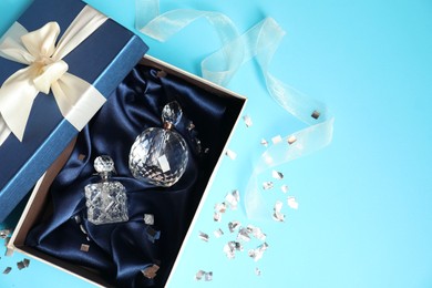 Photo of Perfume bottles in gift box and confetti on light blue background, top view