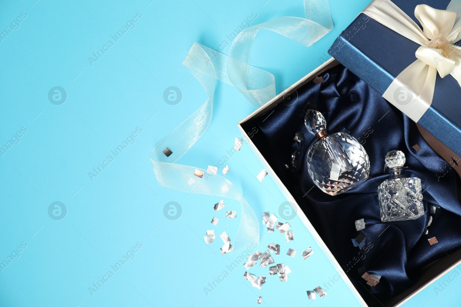 Photo of Perfume bottles in gift box and confetti on light blue background, top view. Space for text