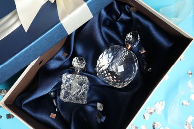 Photo of Perfume bottles in gift box and confetti on light blue background, top view