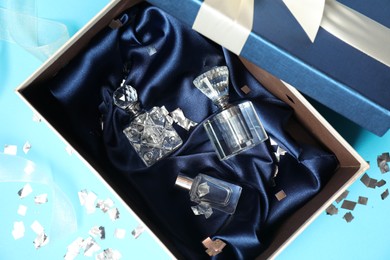 Perfume bottles in gift box and confetti on light blue background, top view