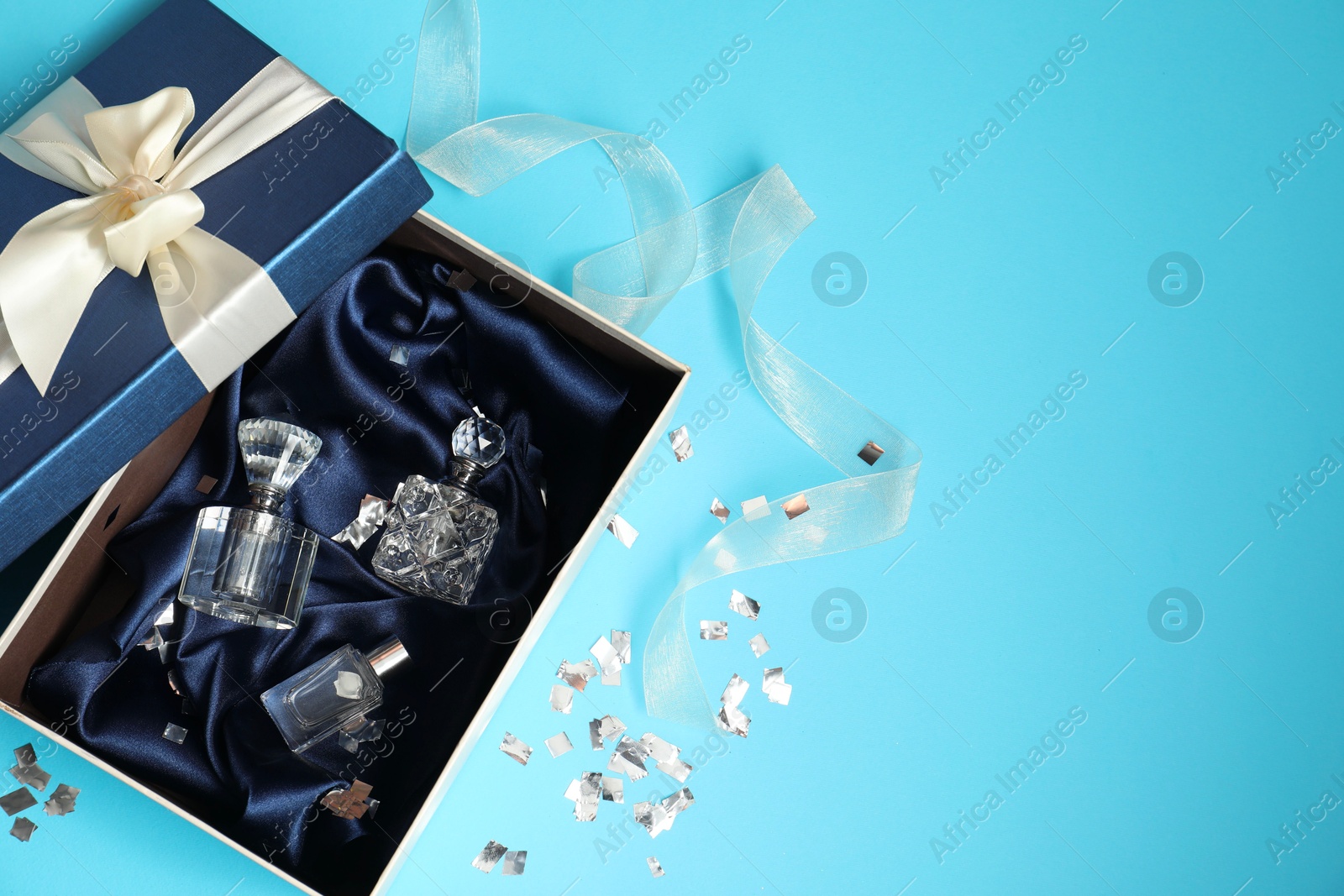 Photo of Perfume bottles in gift box and confetti on light blue background, top view. Space for text