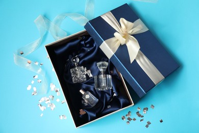 Photo of Perfume bottles in gift box and confetti on light blue background, top view