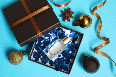 Photo of Perfume bottle in gift box and Christmas decor on light blue background, flat lay