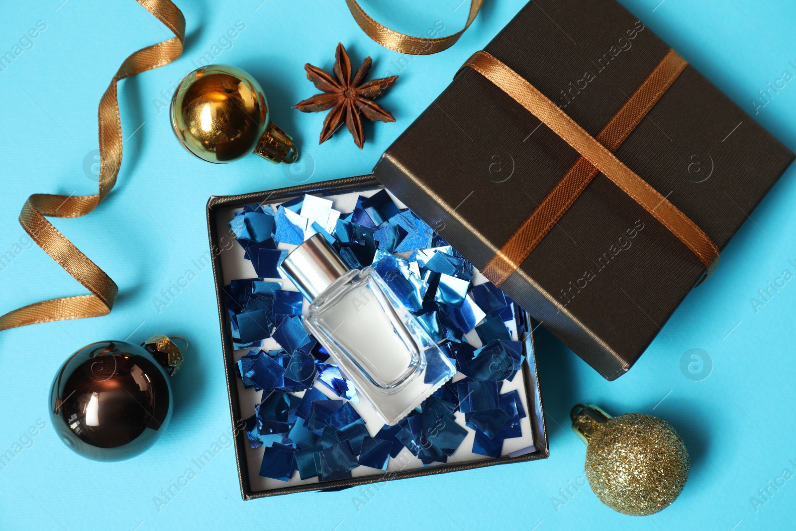 Photo of Perfume bottle in gift box and Christmas decor on light blue background, flat lay