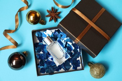 Photo of Perfume bottle in gift box and Christmas decor on light blue background, flat lay