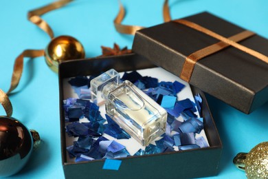 Photo of Perfume bottle in gift box and Christmas decor on light blue background, closeup