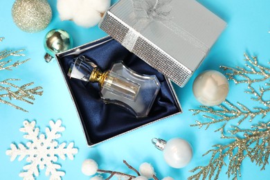 Perfume bottle in gift box and Christmas decor on light blue background, flat lay